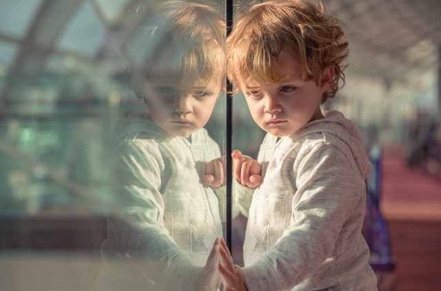 Child standing near window looking bored